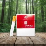 ซองบุหรี่ Dunhill International สีแดง ดีไซน์หรูหรา วางบนโต๊ะไม้ในบรรยากาศป่าสีเขียว