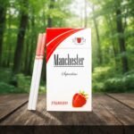 ซองบุหรี่ Manchester Strawberry SuperSlims วางบนโต๊ะไม้ในบรรยากาศป่าธรรมชาติ