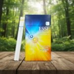 ซองบุหรี่ ESSE Change Double Mango สีน้ำเงินเหลืองลายรัศมี พร้อมมวนบุหรี่สลิมแสดงตำแหน่ง 2 เม็ดบีบ วางบนโต๊ะไม้