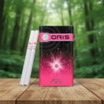 ซองบุหรี่ Oris Intense Summer Fizz สีดำตัดชมพูดีไซน์ลวดลายแผงวงจรดิจิทัล พร้อมมวนสีขาววางบนโต๊ะไม้ฉากหลังป่า