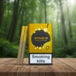 ซองบุหรี่ The King Mango สีเหลืองทองวางบนโต๊ะไม้ฉากหลังเป็นป่าธรรมชาติสีเขียว