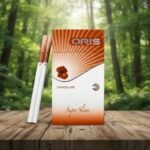 บุหรี่ Oris Chocolate ซองสีน้ำตาลขาวลายรัศมี พร้อมมวนบุหรี่ซุปเปอร์สลิมวางบนโต๊ะไม้ฉากหลังป่า