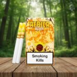 บุหรี่ THIS Africa Rula ซองสีเหลืองลายช้างและยีราฟ รสกล้วยหอมคาราเมล พร้อมมวนบุหรี่วางบนโต๊ะไม้ฉากหลังป่า