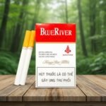 บุหรี่ Blue River Red ซองสีขาวแดง มวนขนาดคิงไซส์ก้นกรองสีส้ม วางบนโต๊ะไม้ฉากหลังป่าธรรมชาติ