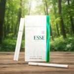 บุหรี่ ESSE Menthol Super Slim ซองสีขาวแถบเขียวมินต์สะท้อนแสง วางคู่กับมวนบุหรี่ซุปเปอร์สลิมบนโต๊ะไม้ฉากหลังป่าธรรมชาติ