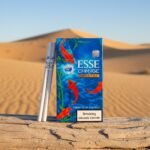 ซองบุหรี่ ESSE Change Special ลายปลาคราฟสีน้ำเงิน วางคู่กับมวนบุหรี่บนขอนไม้ ฉากหลังทะเลทราย