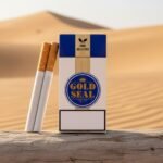 ซองบุหรี่ Goldseal Fine Selected สีขาวน้ำเงิน และมวนบุหรี่ก้นกรองสีน้ำตาล วางบนท่อนไม้ในฉากทะเลทรายสีทอง