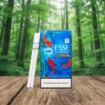 กล่องบุหรี่ ESSE Change Special ลายปลาคราฟสีน้ำเงินสวยงาม วางบนโต๊ะไม้ฉากหลังป่าไม้ธรรมชาติ