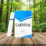ซองบุหรี่ Carnival Blue สีฟ้าขาว วางคู่กับมวนบุหรี่ บนโต๊ะไม้ ฉากหลังป่าธรรมชาติ